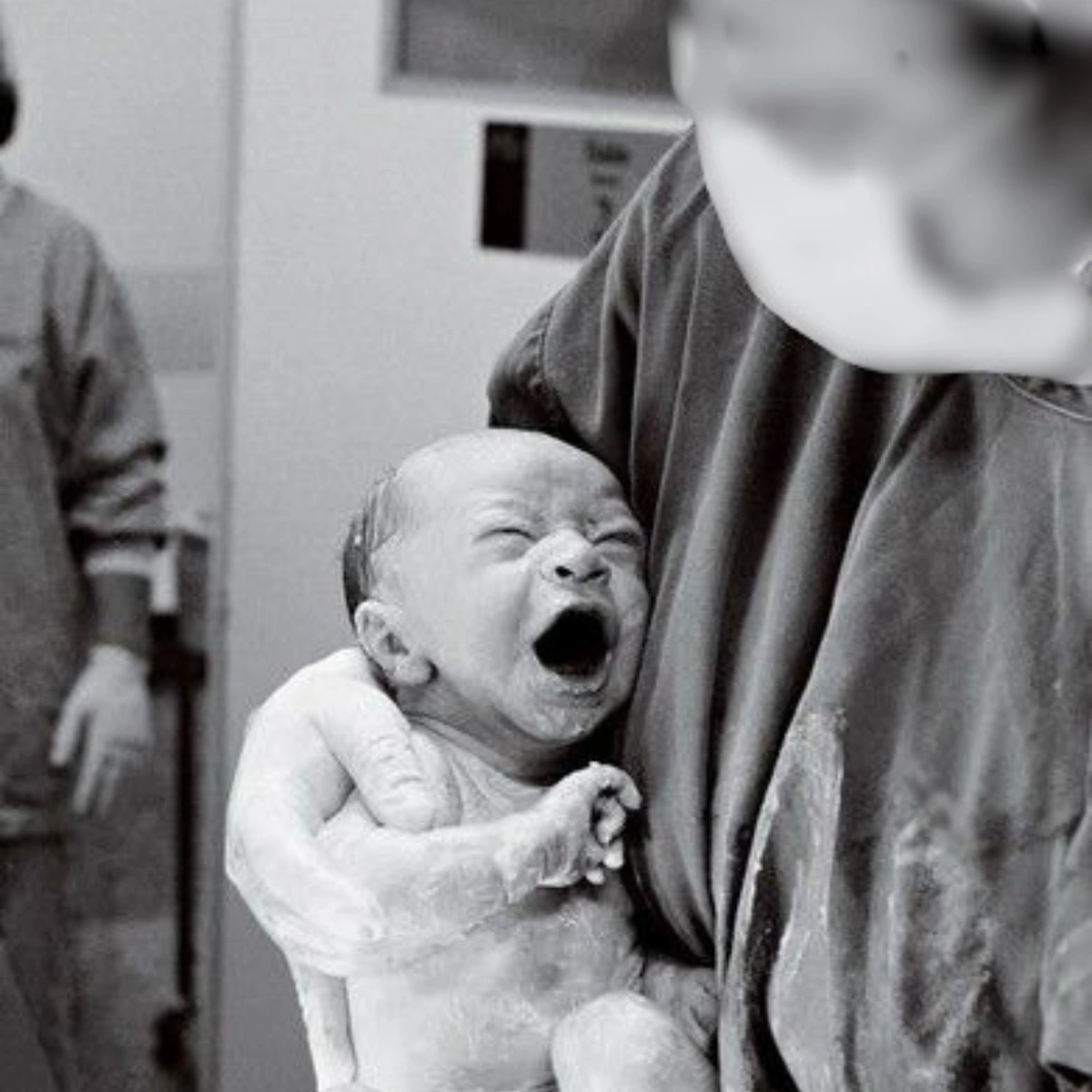 A newborn baby cries in a healthcare professional's arms.